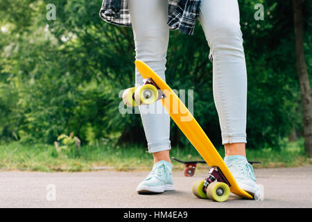 Les jambes des femmes en jeans et baskets sur skateboard jaune libre Banque D'Images