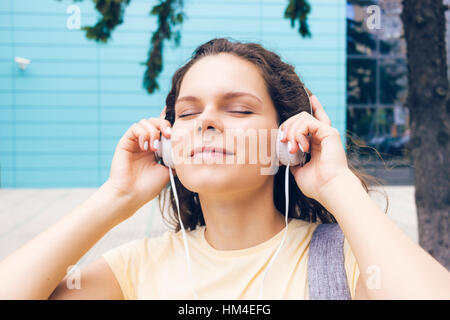 Portrait of a young woman listening to music on headphones avec les yeux fermés dans la ville Banque D'Images