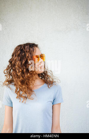 Curly girl à lunettes de soleil et un T-shirt sur le mur à l'arrière-plan, l'espace de copie, l'ossature verticale Banque D'Images