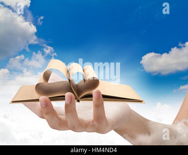 Belle femme hand holding Livre ouvert avec pages de forme de coeur plus de ciel bleu Banque D'Images