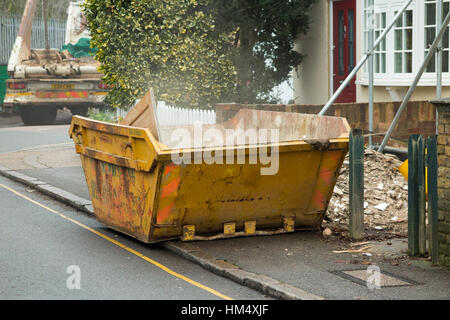 Déchets déchets constructeurs skip, sur la chaussée, la ligne jaune et d'être rempli / chargé builder chargement en camion saute attend. UK Banque D'Images