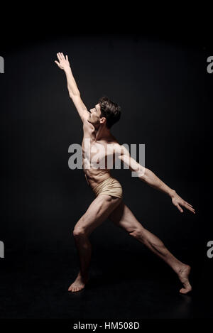 Jeune danseuse enthousiaste qui s'étend dans le studio noir Banque D'Images