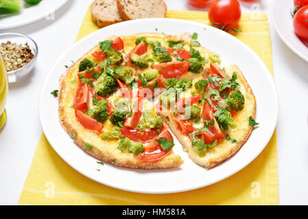 Omelette aux brocolis, tomate, oignon, persil sur plaque blanche, vue en gros plan. Matin, nourriture, lave pour le petit déjeuner Banque D'Images