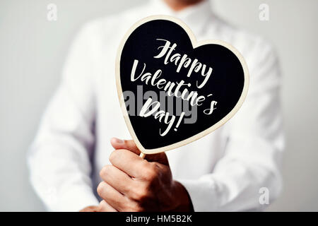 Libre d'un jeune homme de race blanche dans une chemise blanche montrant une pancarte en forme de coeur avec le texte happy valentines day écrit en c Banque D'Images