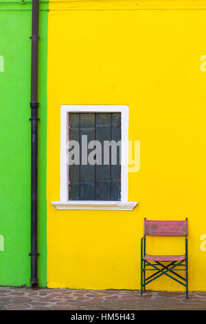 Jeu de chaise contre mur jaune avec des volets aux fenêtres de chambre à Burano - couleurs de Burano, Venise, Italie en janvier Banque D'Images