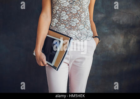 Portrait of businesswoman holding tablet et fichiers debout contre le mur au bureau à domicile Banque D'Images