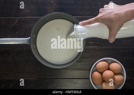 Portrait de mains verser le lait dans le moule par des oeufs sur la table Banque D'Images