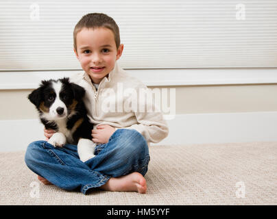 Garçon assis avec chiot sur tapis Banque D'Images