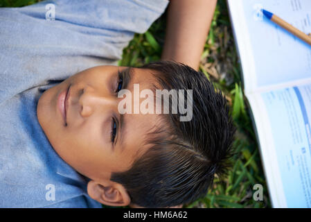 Garçon jeter sur l'herbe avec livre ouvert et un stylo Banque D'Images