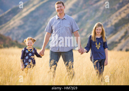 Père de deux filles (4-5, 8-9) walking in field Banque D'Images