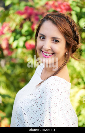 Girl smiling en extérieur dans un parc avec des plantes derrière elle Banque D'Images