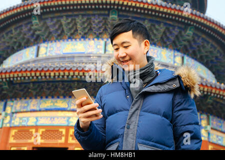 Asian man wearing winter jacket et en utilisant un téléphone intelligent au temple chinois de l'arrière-plan (Selective focus) Banque D'Images