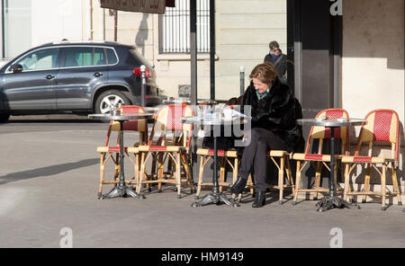 Personnes âgées femme parisien assis à l'extérieur d'un café dans le 6ème arrondissement de Paris en hiver Banque D'Images