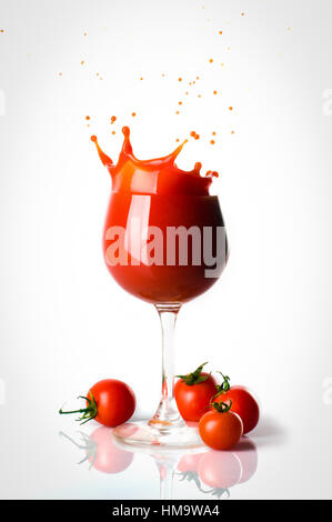 Splash o jus de tomate dans le verre et quatre petites tomates seperated. Banque D'Images