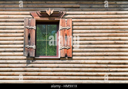 Un fragment d'une maison en bois leurs journaux avec fenêtre et volets en bois. Les fenêtres en verre reflète les arbres verdoyants. Banque D'Images