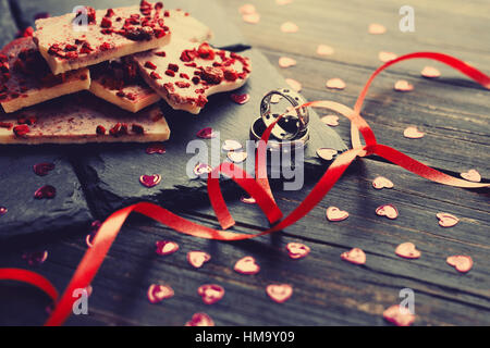 Deux anneaux de mariage et de chocolat blanc avec des framboises séchées sur les plaques en pierre noire, décoré avec des petits cœurs et des rubans rouges, la Saint-Valentin marr Banque D'Images