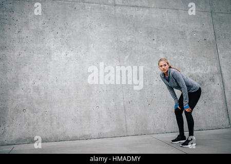 De toute la longueur belle female leaning sur fond gris tout en se reposant après la formation. Athlète femme runner Taking a break avec Banque D'Images