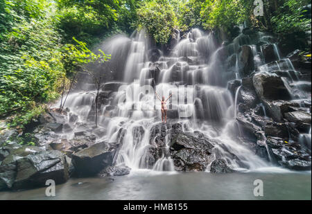 Femme debout sur la roche avec les bras tendus, cascade, Air Terjun Lampo Kanto, près de Ubud, Bali, Indonésie Banque D'Images