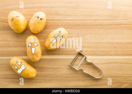 Les pommes de terre fraîches avec cartoon style visages fixant sur une planche à découper et le brun mort de peur d'un couteau économe Banque D'Images