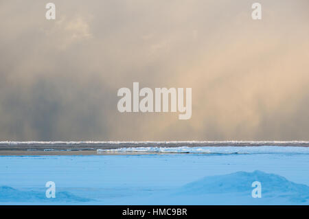 Sidelit nuages de bourrasques de neige en glissant à travers le lac gelé Huron au lever du soleil. La glace flotte sur l'eau calme encore. Banque D'Images