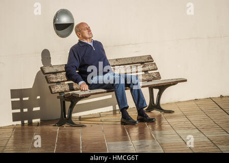 Monsieur plus âgé se détendre au soleil sur un banc. Banque D'Images