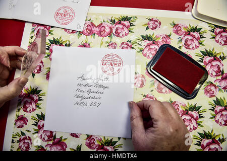 Maîtresse en Chef Lynda Cooper stamps une maquette de carte de Saint-valentin dans le bureau de poste dans le village de Lover, New Forest, où les résidents ont lancé une Saint-valentin post service, permettant aux romantiques dans le monde d'envoyer une carte du village du Wiltshire. Banque D'Images