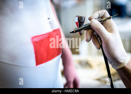 Main tenant la brosse en peinture sur corps femme corps. Artiste pinceau est couvrant le corps avec de la peinture rouge et blanc à l'aide d'un modèle pour faire un tatoo. Banque D'Images