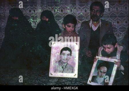 Une famille iranienne posant avec deux grands pans de portraits, l'un d'un jeune homme et l'autre de l'Ayatollah Khomeini, Mars, 1983. Deux femmes en niqab voiles et d'un homme dans un costume de l'ouest s'asseoir sur le sol encadrant deux petits garçons maintenant les photos. D'importants dégâts sur l'original. (Photo de la Collection Morse/Gado/Getty Images). Banque D'Images