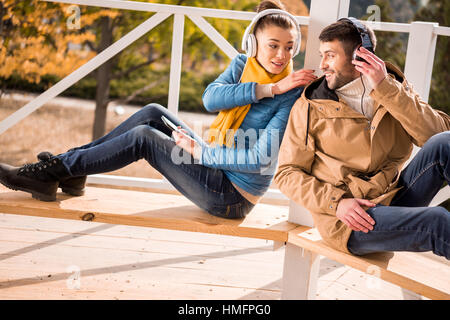 Young couple sitting on bench in headphones Banque D'Images
