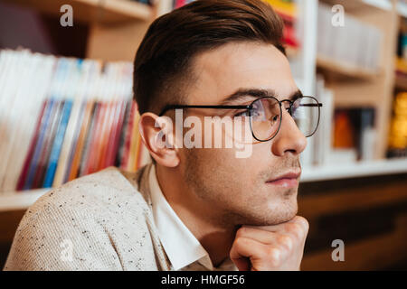 Image of young man wearing eyeglasses sitting in cafe tout en regarder de côté. Banque D'Images