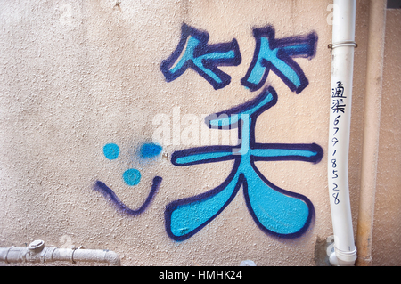 Caractère chinois pour smile écrits en bleu graffiti sur un mur à Hong Kong Banque D'Images