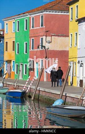 Couple en train de marcher le long des rues maisons colorées avec des bateaux et des réflexions à Burano - couleurs de Burano, Venise, Italie en janvier Banque D'Images