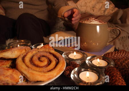 Détente sur une soirée d'hiver aux chandelles dans un cadre chaleureux, hygge inspiré, English salon avec plateau, une couverture, un livre et des pâtisseries Banque D'Images