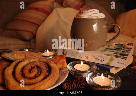 Un confortable coin,bougie allumée dans une maison anglaise inspirée par le concept danois de hygge avec viennoiseries, boisson chaude,un bon livre, une couverture et un canapé confortable Banque D'Images