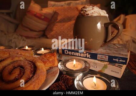 Un confortable coin,bougie allumée dans une maison anglaise inspirée par le concept danois de hygge avec viennoiseries, boisson chaude, un livre, une couverture et un canapé confortable Banque D'Images