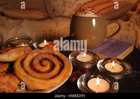 Un confortable coin,bougie allumée dans une maison anglaise inspirée par le concept danois de hygge avec viennoiseries, boisson chaude,un bon livre, une couverture et un canapé confortable Banque D'Images