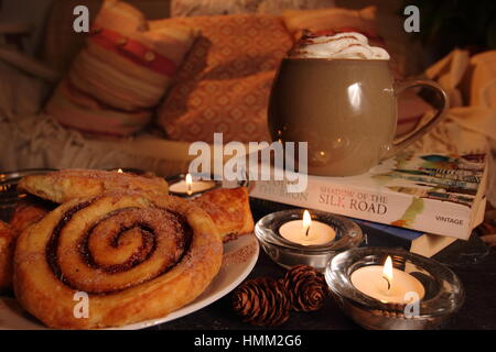 Un confortable coin,bougie allumée dans une maison anglaise inspirée par le concept danois de hygge avec viennoiseries, boisson chaude,un bon livre, une couverture et un canapé confortable Banque D'Images