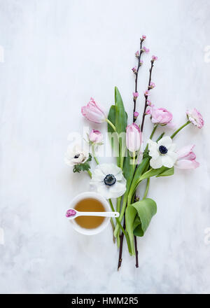 Mise à plat des fleurs de printemps organisées autour d'un verre sur un fond gris et blanc peint, style photographié en lumière naturelle Banque D'Images