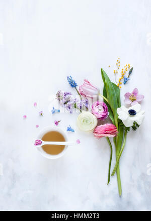 Mise à plat des fleurs de printemps organisées autour d'un verre sur un fond gris et blanc peint, style photographié en lumière naturelle Banque D'Images