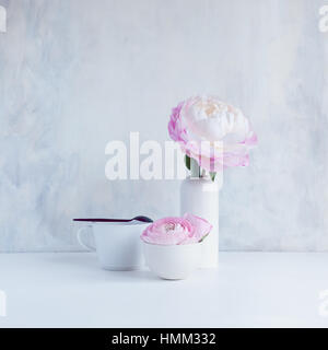 Still Life of pink ranunculus dans Bol en céramique blanche et rose pivoine en blanc petit vase en céramique avec tasse et cuillère Banque D'Images