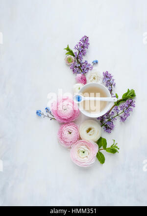 Mise à plat des fleurs de printemps et d'un verre peint en blanc et gris style toile et photographié en lumière naturelle Banque D'Images