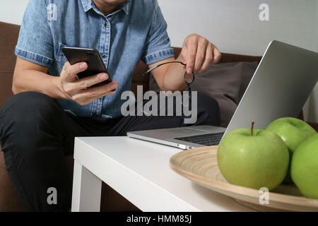La main à l'aide d'hipster coffre compter les paiements mobiles et les entreprises en ligne, lunettes,sitting on sofa in living room,pomme verte en plateau en bois Banque D'Images