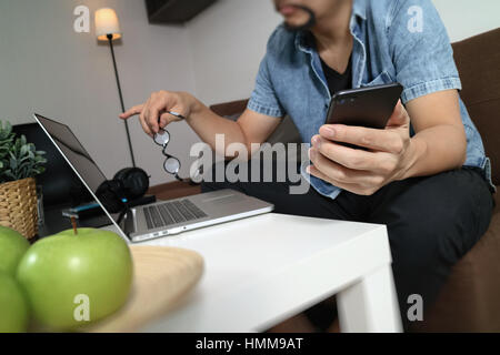 La main à l'aide d'hipster coffre compter les paiements mobiles et les entreprises en ligne, lunettes,sitting on sofa in living room,pomme verte en plateau en bois Banque D'Images