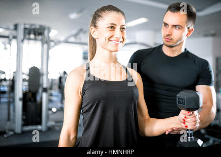 Young adult woman working out in gym, faire des biceps avec l'aide de son entraîneur personnel. Banque D'Images