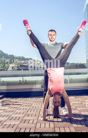 Femme fitness féminin doing handstand, tandis que son entraîneur personnel prend en charge sa. Banque D'Images