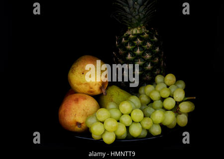 Poires, raisins et ananas disposées sur une plaque noire avec Rembrandt l'éclairage. Banque D'Images