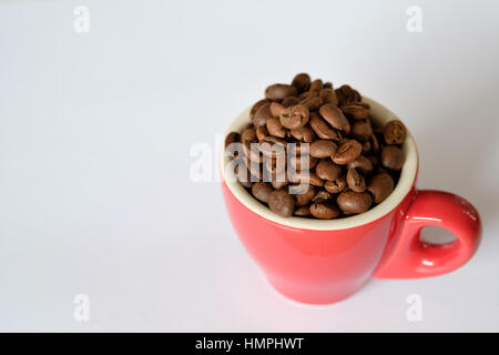 Grains de café dans une tasse à espresso rouge sur fond blanc Banque D'Images