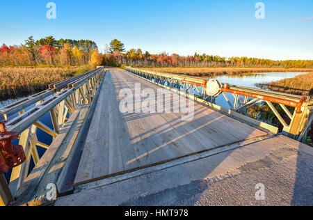 Vue grand angle du ciel bleu clair, la fin de l'après-midi, soleil jette de longues ombres sur un pont en bois et d'acier léger, seul point sur une perspective lak Banque D'Images