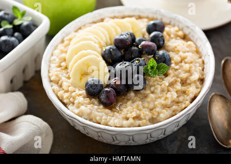 Couper l'acier du porridge d'avoine avec bananes et myrtilles pour le petit déjeuner Banque D'Images