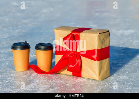 Cadeaux artisanat avec ruban rouge et tasses de café sur la patinoire. Banque D'Images